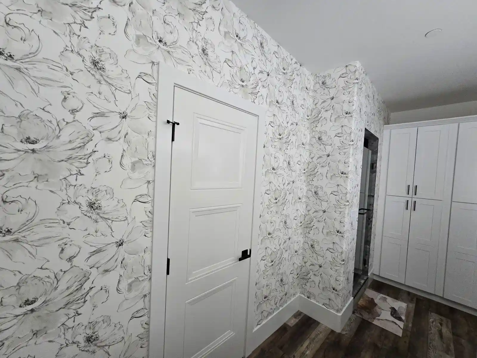 Bright white hallway with oversized black line-drawn floral wallpaper, a sliding door and dark wood flooring.