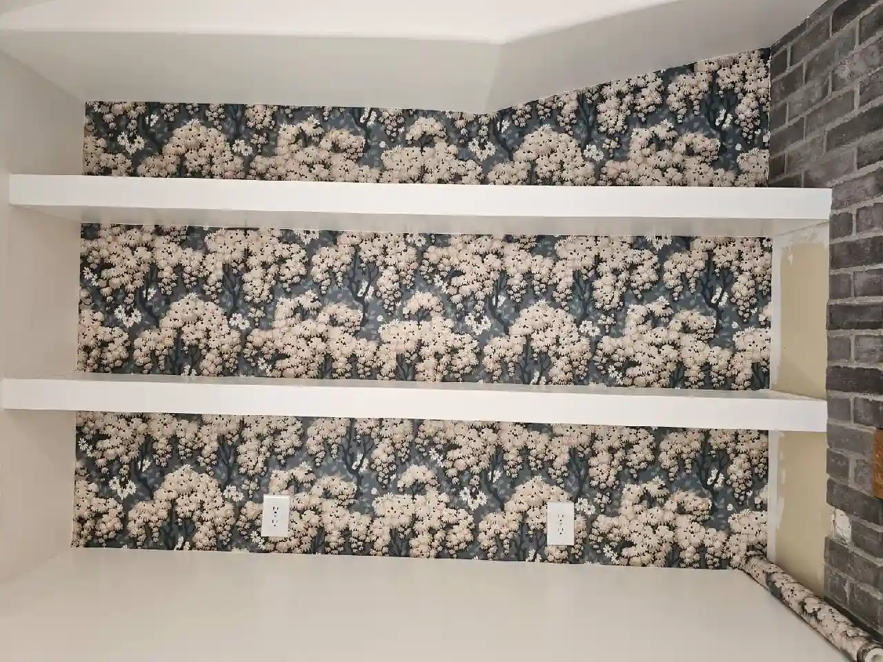 Dark floral wallcovering inside a white shelving recess, with a matching roll resting on the lower ledge.