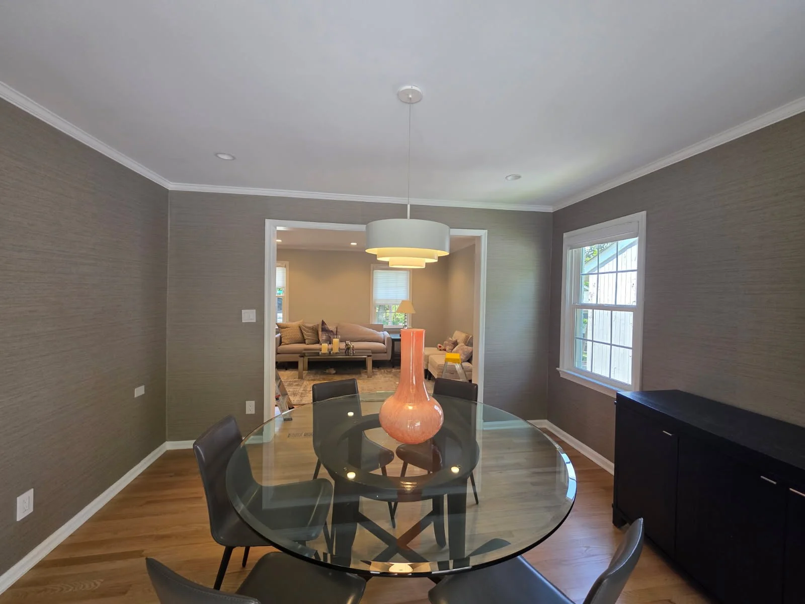 Dining room with a round glass table, black chairs and subtle taupe textured wallcovering.